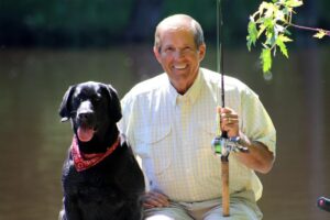 Ron Schara and his dog Raven are posing for a photo. Ron is holding a fishing rod.