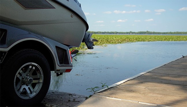 A boat is being towed in the bed of a truck and is being lowered onto a landing to launch it.
